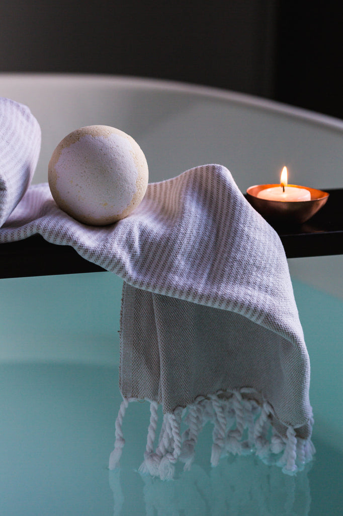 Photo of a bath tub with a tray on top with a towel, candle and bath bomb